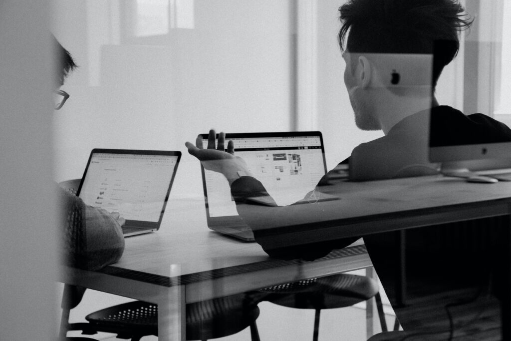 Two employees in the finance team sitting with laptops to discuss the risks of outsourcing finance