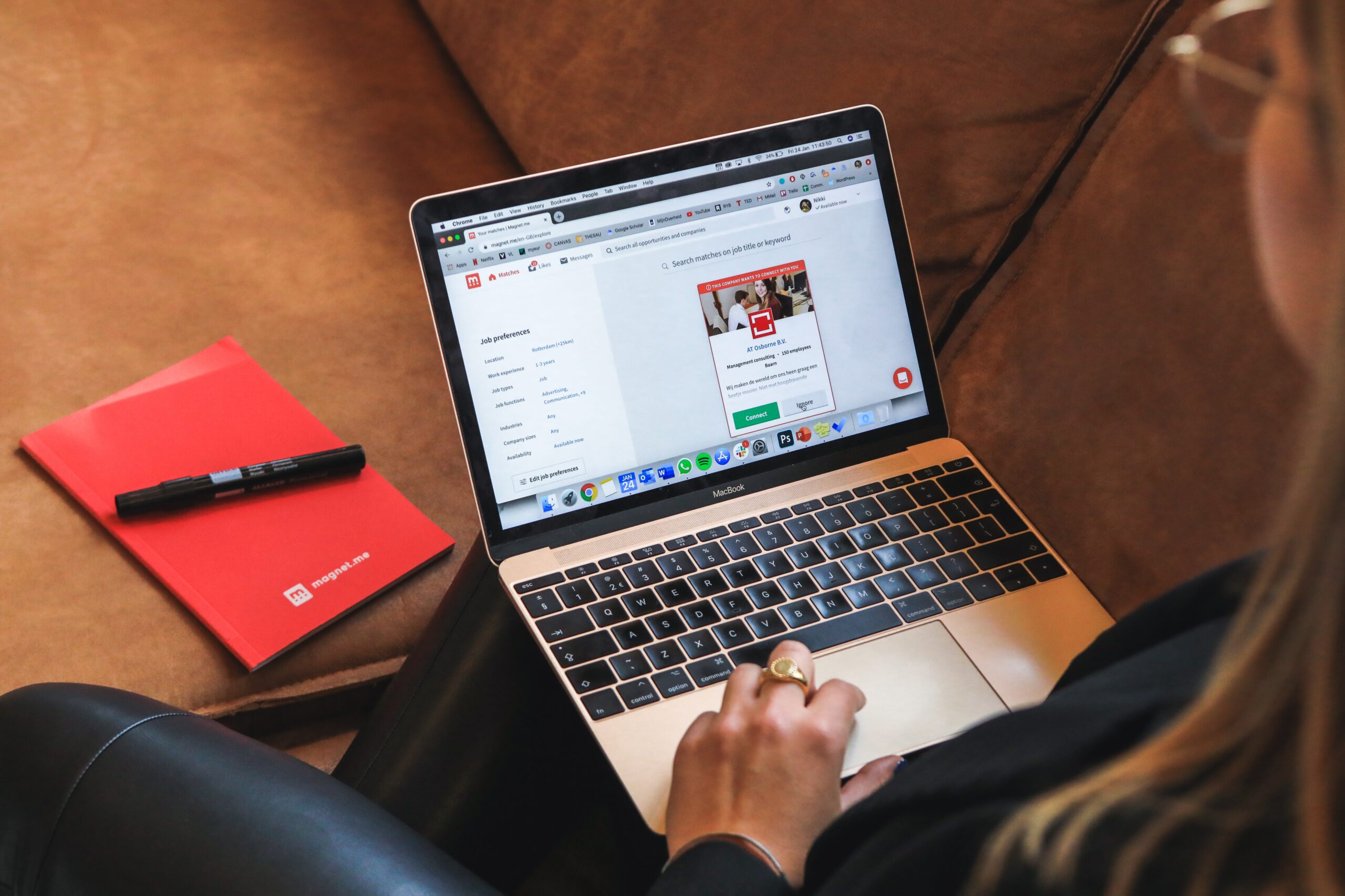 A female professional getting a job offer for global hiring and working remotely on a laptop with a red notebook and pen